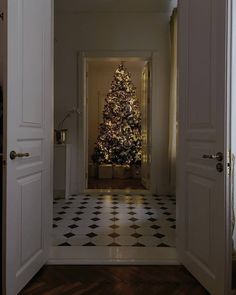 an open door leading to a decorated christmas tree in a room with black and white checkered flooring