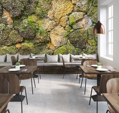 a stone wall with moss growing on it is shown in this restaurant setting, complete with wooden tables and chairs