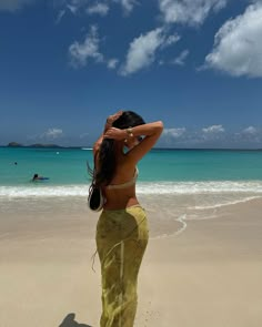 a woman standing on top of a sandy beach next to the ocean with her hands behind her head