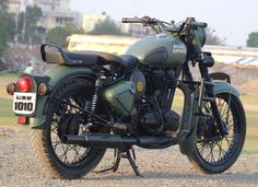 a green motorcycle parked on top of a gravel field