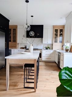 a kitchen with white cabinets and wooden floors is pictured in this image, there are two hanging lights above the island