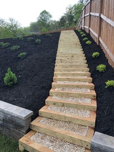 a set of wooden steps leading up to a fenced in area with black mulch