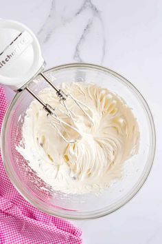 a mixing bowl filled with whipped cream on top of a pink and white checkered towel