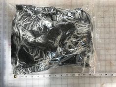 a plastic bag filled with black and white hair on top of a table next to a ruler