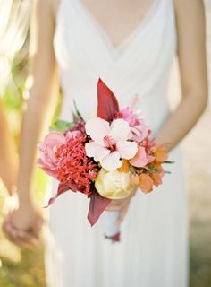 a woman in a white dress holding a pink and orange bouquet with her hands behind her back