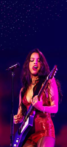 a woman holding a guitar while standing in front of a microphone