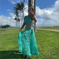 a woman standing next to a palm tree wearing a green skirt and cropped top