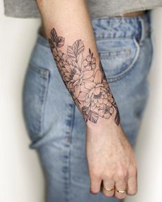 a woman's arm with flowers on it and leaves around the wrist, in front of her