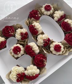 two dozen cupcakes with red and white frosting roses in a heart shaped box