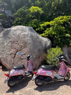 two pink scooters parked next to each other in front of a large rock