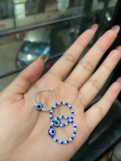 a person's hand holding two rings with evil eyes on them and blue beads