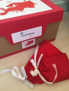 a red bag sitting on top of a wooden floor next to a box with a white ribbon