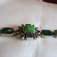 "Sterling silver link bracelet with two amethyst faceted stones and various green stones. There are dark green cushion cut stones, lime green cabs, and two colors of faceted small marquis stones. Some look like peridot. Stamped IB India 925. The center cluster is 1\" tall x 1 1/8\" wide. The length of the bracelet is 8\". Lobster claw clasp. Good condition. Shipped by US mail. LB-1" Unique Green Gemstones For Formal Occasions, Adjustable Green Amethyst Jewelry, Modern Green Jewelry With Gemstone Accents, Rectangular Green Jewelry With Natural Stones, Green Rectangular Jewelry With Natural Stones, Green Faceted Bracelet, Formal Green Amethyst Jewelry, Rectangular Green Natural Stone Jewelry, Green Rectangular Natural Stone Jewelry