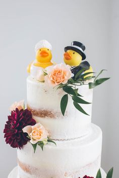 a wedding cake decorated with flowers and rubber ducky figurines sitting on top