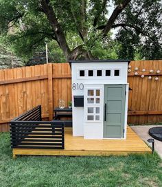 a small white shed sitting on top of a wooden platform next to a green fence