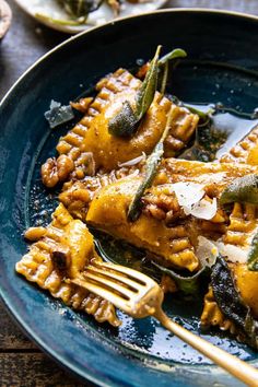 a blue plate topped with pasta covered in sauce and cheese next to a fork on top of a wooden table