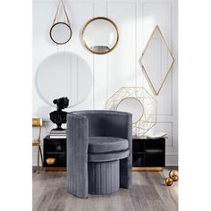 a room with white walls, gold accents and grey velvet chair in the corner next to a round mirror