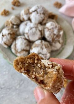 a hand holding a half eaten cookie in front of a plate of cookies and powdered sugar