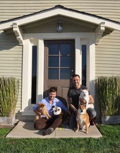 two men sitting in front of a house with three dogs and one cat on the porch