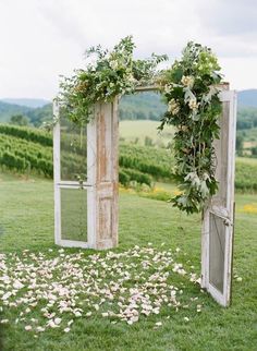 an outdoor ceremony setup with flowers and greenery on the grass in front of two open doors