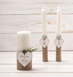 two white candles are sitting next to each other with hearts and initials on the candle holders