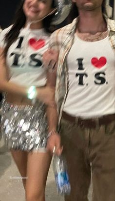 the man and woman are dressed up in disco outfits, one is wearing a silver sequin skirt while the other wears a t - shirt that says i love biss