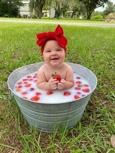 a baby sitting in a tub filled with water and strawberries, smiling at the camera