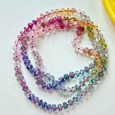 multicolored glass beaded necklaces next to a yellow plastic object on a white surface