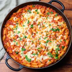 a skillet filled with pasta and sauce on top of a wooden table