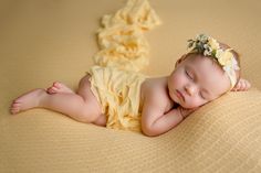 a sleeping baby wearing a yellow dress and flower headband on top of a blanket