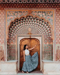 a woman standing in front of a wooden door wearing a long skirt and crop top