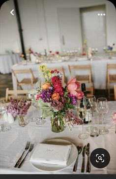 the table is set with white linens and flowers in vases, silverware, and wine glasses