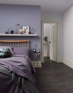 a bedroom with purple walls and wood flooring is pictured in this image, the bed has two pillows on it