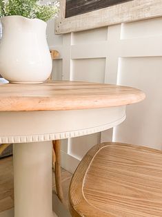 a white vase sitting on top of a table next to a wooden bench and chair