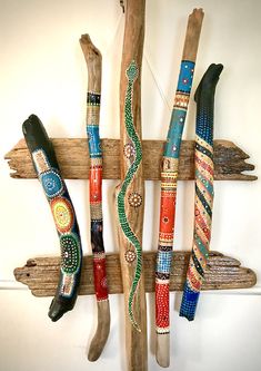 three wooden sticks with painted designs on them hanging from a wall next to another piece of driftwood