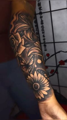 a woman's arm with black and white tattoos on her forearm, holding flowers