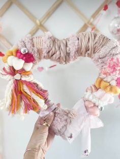 a person holding up a wreath made out of yarn and other items in the shape of a heart