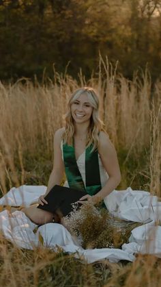 a woman sitting on a blanket in the middle of a field with tall grass and flowers