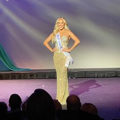 a woman standing on top of a stage in front of a crowd wearing a crown