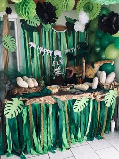 a table topped with lots of green and white balloons next to a wall covered in palm leaves