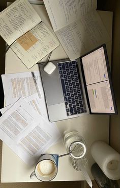 an open laptop computer sitting on top of a desk next to papers and a cup of coffee