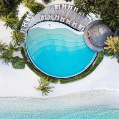 an aerial view of a resort pool surrounded by palm trees and blue water in the ocean