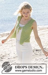 a woman is walking on the beach in white pants and a green crochet vest