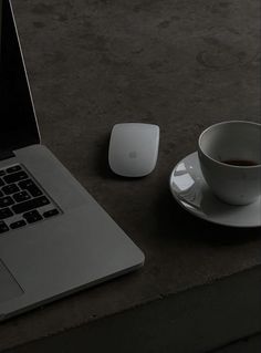 a cup of coffee sits next to an apple mouse and macbook pro on a table