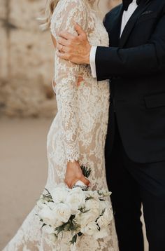 a bride and groom embracing each other in front of a stone wall with white flowers