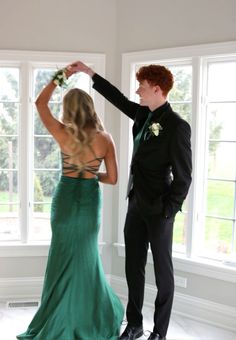 a young man and woman in formal wear standing next to each other near two windows