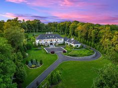 an aerial view of a large white house surrounded by trees and lush greenery at sunset