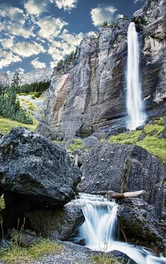 a waterfall in the mountains with rocks and grass