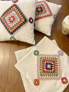 three white pillows with colorful crocheted designs on them sitting on a wooden floor