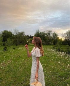 a woman in a white dress is holding a flower and looking up at the sky